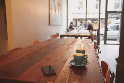 Two espresso cups and a phone on a wooden café table