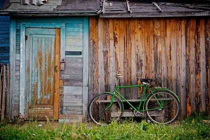 A green bicycle leaned against a weathered wooden shed